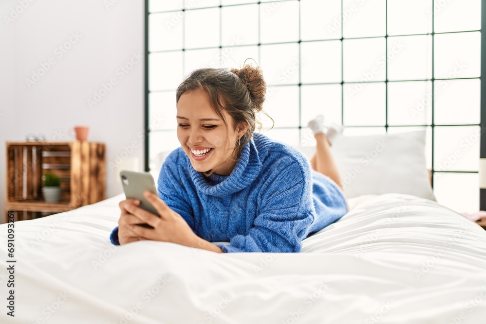 Poster Young beautiful hispanic woman using smartphone lying on bed at bedroom