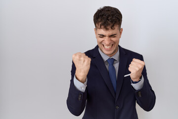 Young hispanic business man wearing suit and tie very happy and excited doing winner gesture with arms raised, smiling and screaming for success. celebration concept.