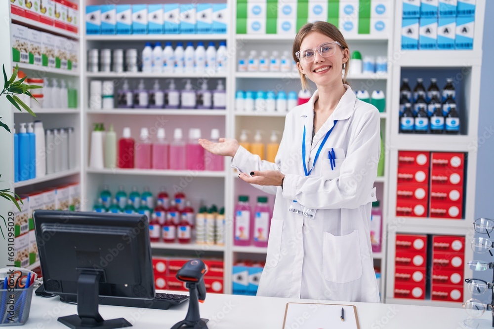 Wall mural Young blonde woman pharmacist smiling confident presenting at pharmacy