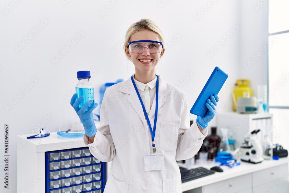 Poster Young blonde woman scientist using touchpad holding bottle with liquid at laboratory