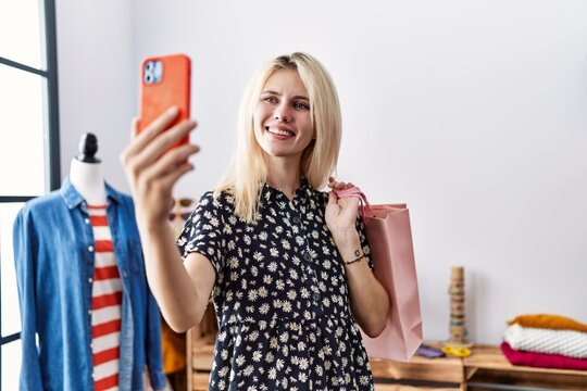 Young blonde woman holding shopping bags make selfie by smartphone smiling at clothing store