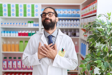 Hispanic man with beard working at pharmacy drugstore smiling with hands on chest with closed eyes...