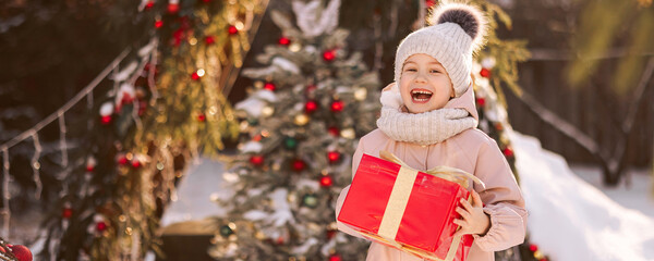 Little girl with a Christmas gift outdoors in winter on Christmas Eve. New Year background for holiday sale or promotion. Banner with copy space.