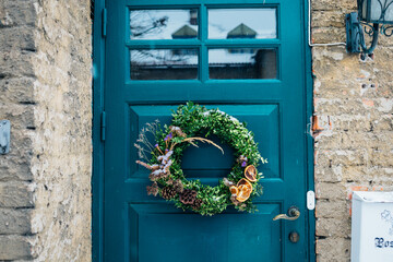 Beautiful entrance to scandinavian style house with wooden door and christmas wreath. Homemade diy xmas decoration. Winter city doors and landscape. Inspiring winter ornaments and nordic lifestyle