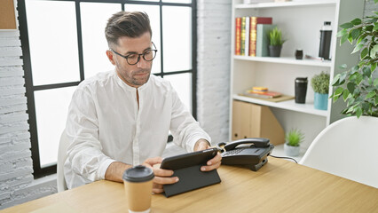 El jefe, portrait of a young, handsome hispanic man seriously working on his touchpad device at his...