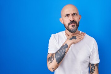 Hispanic man with tattoos standing over blue background cutting throat with hand as knife, threaten...