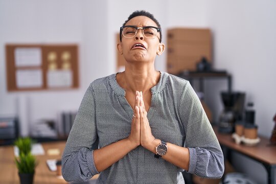African american woman working at the office wearing glasses begging and praying with hands together with hope expression on face very emotional and worried. begging.