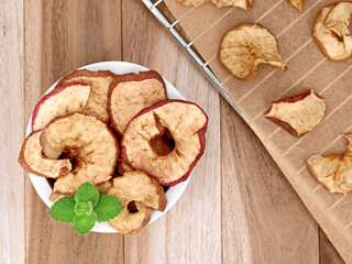 Dried apple rings in white bowl on a wooden table, homemade apple rings on a baking tray from the oven