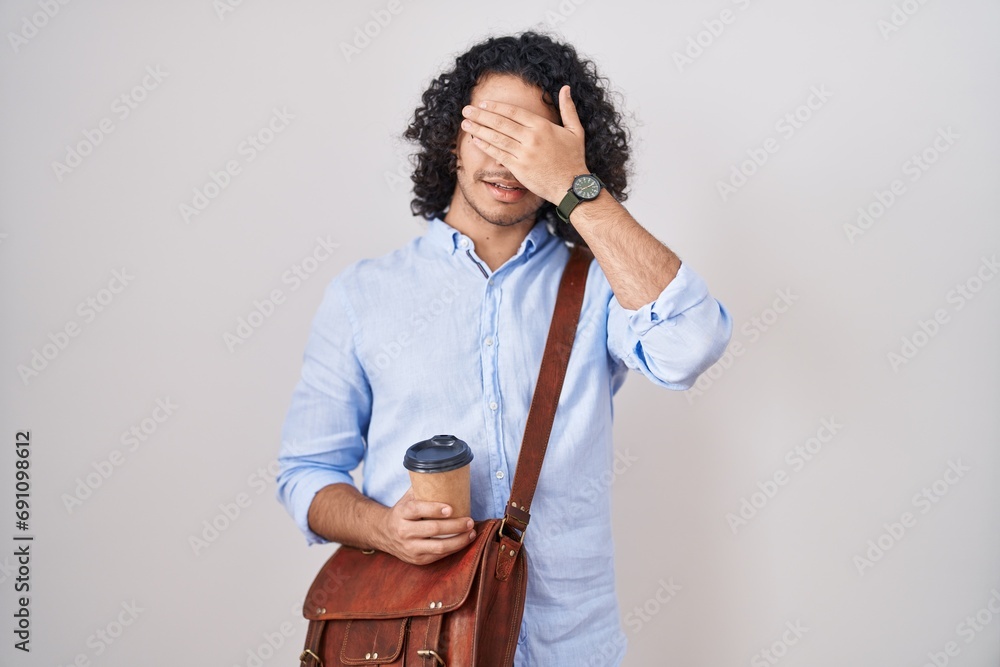 Canvas Prints Hispanic man with curly hair drinking a cup of take away coffee smiling and laughing with hand on face covering eyes for surprise. blind concept.