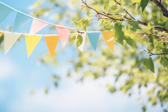 Vibrant bunting adornment in verdant tree leaves against azure sky, summertime celebration backdrop design with room for text.