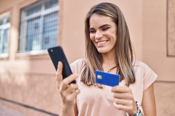 Naklejka premium Young beautiful hispanic woman using smartphone and credit card at street