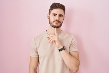 Hispanic man with beard standing over pink background thinking concentrated about doubt with finger...
