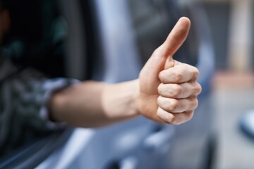 Young caucasian man driving car doing ok gesture with thumb up at street