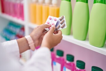 Young beautiful hispanic woman pharmacist holding pills tablets at pharmacy