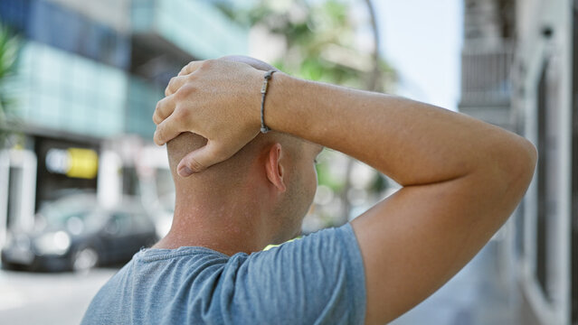 Young hispanic man standing backwards touching head at street