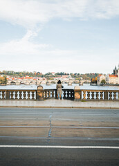 Female traveler dressed in gray coat standing on the bridge above Vltava river in Prague (Czech Republic) and looking on Charles Bridge - photo from her back. Wide- angle shot of woman turist in city.