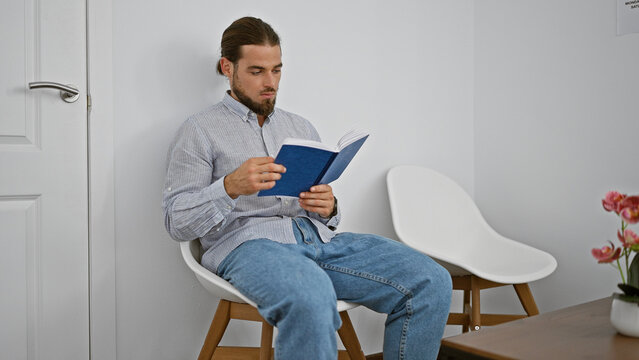 Young hispanic man reading book sitting on chair at waiting room