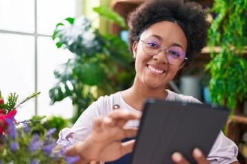 African american woman florist smiling confident using touchpad at flower shop