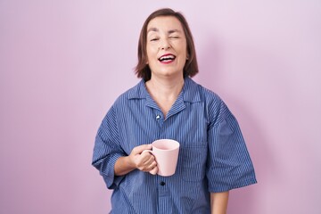 Middle age hispanic woman drinking a cup coffee winking looking at the camera with sexy expression,...