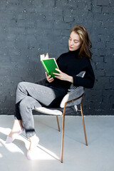 a full-length vertical side photo of a concentrated young woman sitting in chair and reading a...