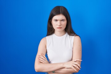 Young caucasian woman standing over blue background skeptic and nervous, disapproving expression on face with crossed arms. negative person.