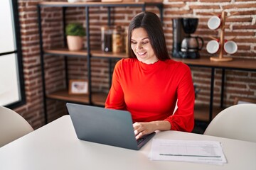 Young beautiful hispanic woman using laptop sitting on table at home