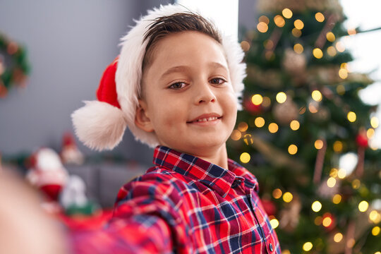 Adorable hispanic boy make selfie by camera standing by christmas tree at home