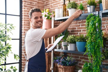 Young hispanic man florist holding plant and clipboard at florist - obrazy, fototapety, plakaty