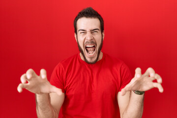 Young hispanic man wearing casual red t shirt smiling funny doing claw gesture as cat, aggressive...