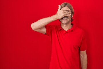 Caucasian man with mustache standing over red background smiling and laughing with hand on face...