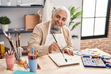 Middle age grey-haired man artist smiling confident drawing on notebook at art studio