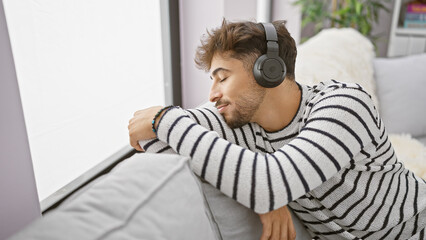 Young arab man enjoys his own sound sanctuary, relaxed on sofa, engrossed in the audio technology...