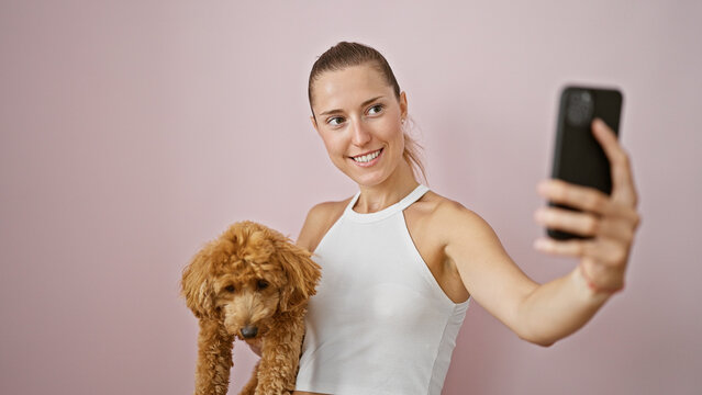 Young caucasian woman with dog smiling hugging taking selfie photo with smartphone over isolated pink background