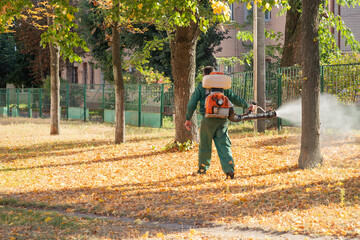 Worker sprays territory with insecticide for mosquitoes or pests or herbicides for weeds. - obrazy, fototapety, plakaty