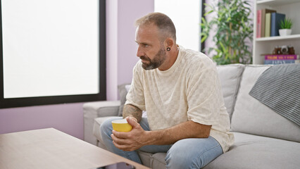 Handsome young man in deep thought, sitting comfortably at home, sipping coffee on a relaxing morning.
