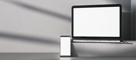 Close up of empty white laptop and mobile phone on gray desk. Concrete wall background, shadows and pedestal or podium. Device presentation and online education concept. Mock up, 3D Rendering.