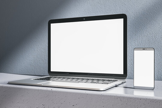 Close up of empty white laptop and cellphone on gray desk. Concrete wall background. Device presentation and online education concept. Mock up, 3D Rendering.