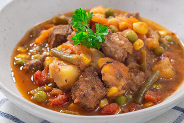 Vegetable beef stew with potato, green beans, carrot, peas and corn, in gray bowl, horizontal, closeup