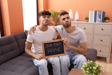 Homosexual gay couple holding blackboard with first home text looking at the camera blowing a kiss...