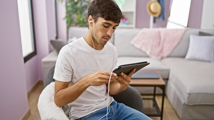Handsome young hispanic man totally engrossed, watching a captivating video on his touchpad,...
