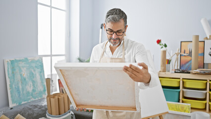 Confident, smiling young hispanic man, grey-haired artist at work, engrossed in drawing, reveling...