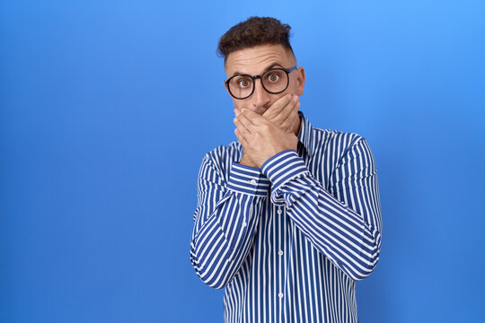 Hispanic man with beard wearing glasses shocked covering mouth with hands for mistake. secret concept.