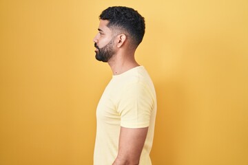 Hispanic man with beard standing over yellow background looking to side, relax profile pose with natural face and confident smile.