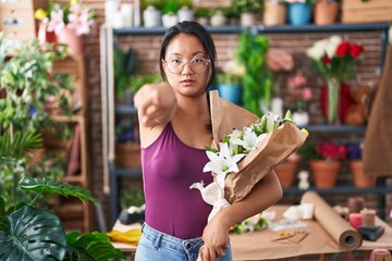 Asian young woman at florist shop holding bouquet of flowers pointing with finger to the camera and...