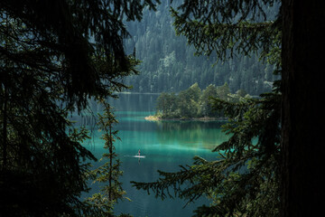 View through trees of the German mountain lake Eibsee with clear water and person on their stand up paddle board.
