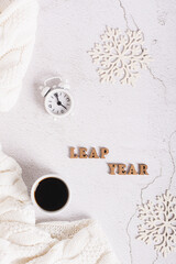 Leap year concept, coffee, alarm clock, snowflakes and letters on a light top and vertical view
