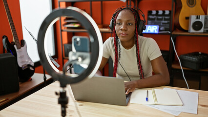 Smiling african american woman reporter broadcasts live, speaking with headphones during video call...