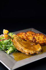 poultry meat with sauce served with hash browns and salad