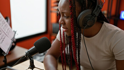 Confident african american woman reporter in braids, speaking on air at an indoor music studio,...