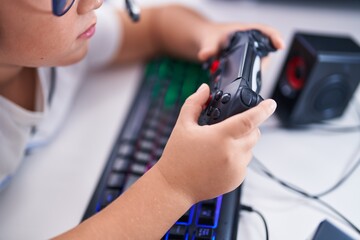 Adorable hispanic boy streamer playing video game using joystick at gaming room